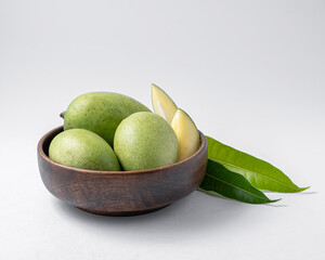 natural raw or green mangos or aam in a wooden bowl with green mango leaves on a white background useful for packaging or editorial purpose