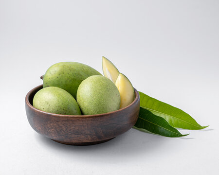 natural raw or green mangos or aam in a wooden bowl with green mango leaves on a white background useful for packaging or editorial purpose
