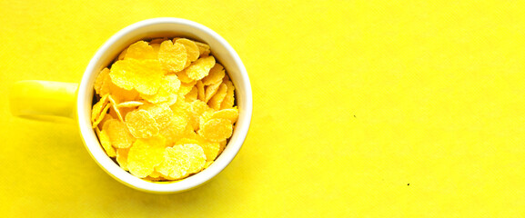 Yellow cup with cornflakes on bright yellow background.