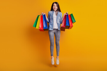 Portrait of active positive girl jumping hold shopping bargains isolated on yellow background