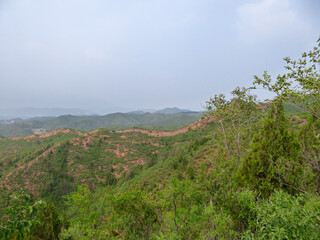 A panoramic view on an unrenewed Gubeikou part of Great Wall of China. The wall is spreading on tops of mountains. Many watchtowers on the peaks. Dense forest around it. World wonder. Tradition