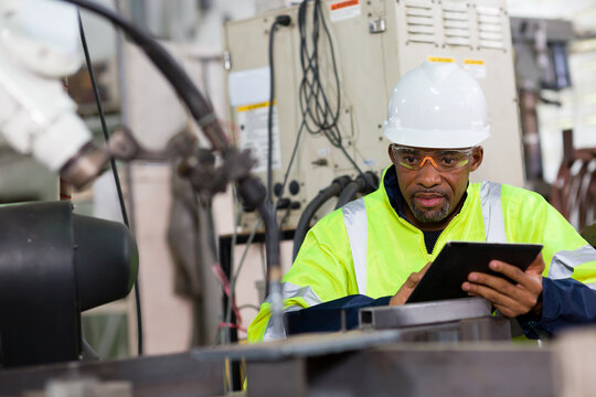 African American male engineer worker using tablet with the automatic robotic machine in the factory. Black male technician worker working with control automatic robot arm system welding
