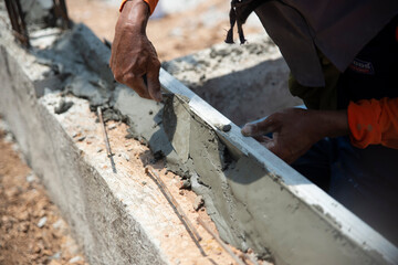 Closeup hands of the workers were plastering cement concrete on the walls with trowel at house construction site.