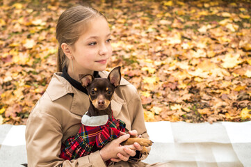 Teenage girl holding a small dog in her arms against a background of yellow autumn foliage