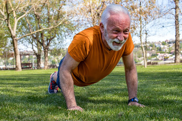 Portrait of a senior man exercising, doing push ups in the park. An elderly man in good shape with strong arms.