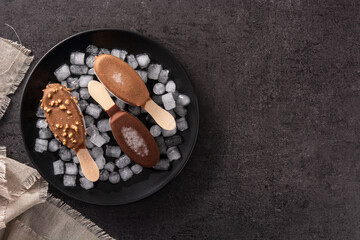 Chocolate popsicles and crushed ice on black stone. Top view. Copy space
