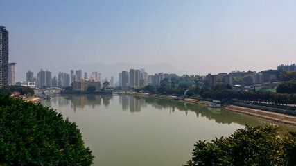 Obraz premium A panoramic view on the skyline of Fuzhou, China. The skyscrapers are reflecting in the Min River. The river has brownish color. Clear and blue sky. Modern, developed city. Thick forest on the sides