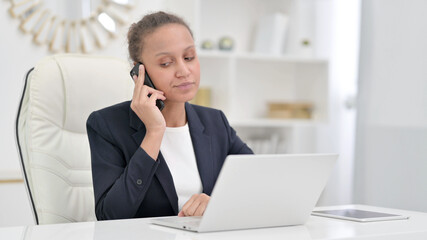 Fototapeta premium African Businesswoman with Laptop Talking on Phone in Office 