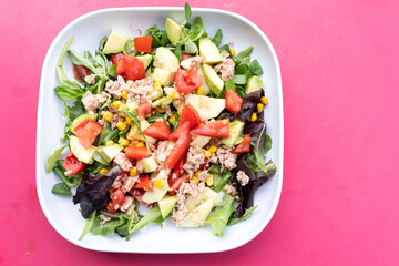 Ensalada de aguacate y verduras en plato sobre fondo rosa, comida vegetariana saludable y divertida