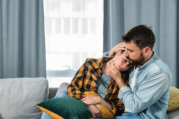 Young couple is lying on the sofa because the woman has menstruation and her stomach hurts and the guy hugs and comforts her to relieve her pain and suffer of female issues 