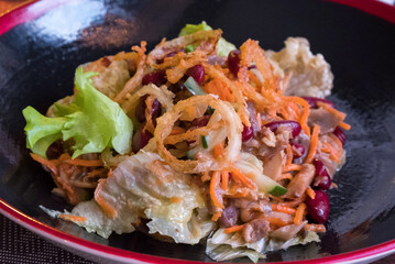Delicious Asian salad on a black plate. Red beans, meat, lettuce and other ingredients