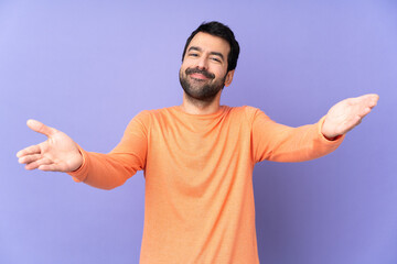 Fototapeta premium Caucasian handsome man over isolated purple background presenting and inviting to come with hand