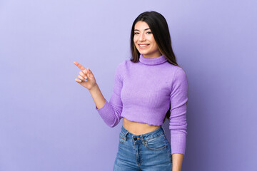 Young brunette woman over isolated purple background pointing finger to the side