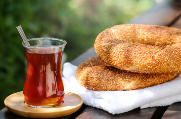 Traditional Turkish sesame bagel simit and Turkish tea on wood background with hard sun light shadows on. street food. Tasty breakfast. Nature background