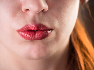 Close-up of a young woman's lips painted with red lipstick. Beautiful plump lips. Lip texture. Kiss of a young woman. Background - bright red hair