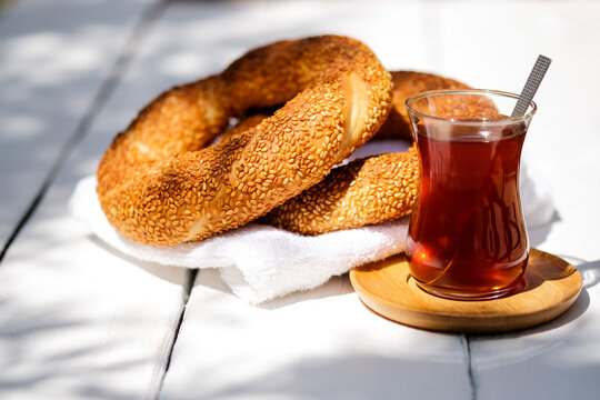 Traditional Turkish sesame bagel simit and Turkish tea on white wood background with hard sun light shadows on street