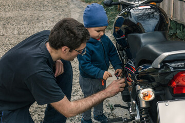 Dad and son at work. A young son helps his dad repair a motorcycle on the street. Communication between father and son.