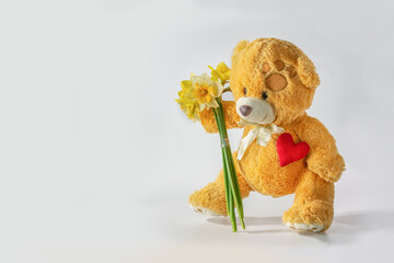 Photo postcard with a picture of a funny teddy bear with a bunch of daffodils and a red heart on a light background.