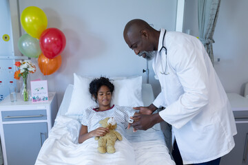African american male doctor putting pulse oximeter on sick mixed race girl in hospital bed