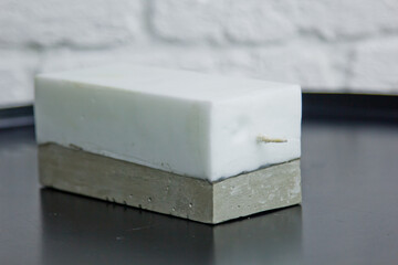 homemade white candle with concrete on the background of a white wall. handmade decor close-up. Details of colored candles in the loft style in the shape of a cube