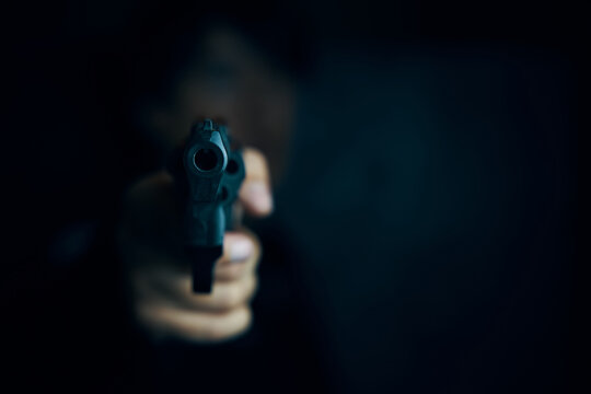 Muzzle of gun in man's hand is pointed at camera. Threat of firearms. Male criminal holds revolver on black background. Attack or defense.