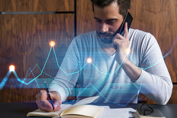 Handsome analyst in casual long sleeve talking phone, taking notes at office workplace try to find...