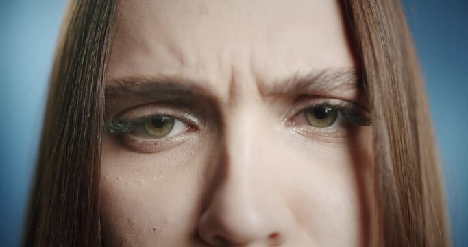 Portrait of young woman frowning, looking in camera with displeased face. Close-up of female model student with green eyes, having angry view.