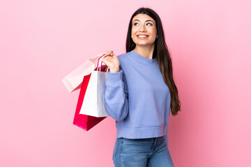 Fototapeta na wymiar Young brunette girl over isolated pink background holding shopping bags and smiling