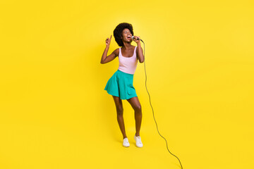 Full size photo of dark skin funky woman sing song karaoke enjoy music wear pink tank-top isolated on yellow color background
