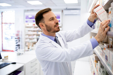 Naklejka na ściany i meble Pharmacist working in pharmacy store and arranging boxes of medicines on the shelf.