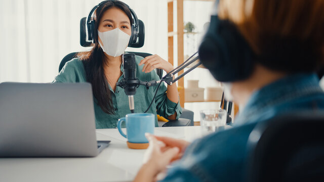 Asia girl radio host record podcast use microphone wear headphone interview guest content wear mask protect virus conversation talk and listen in her room. Podcast from home, coronavirus quarantine. - Powered by Adobe