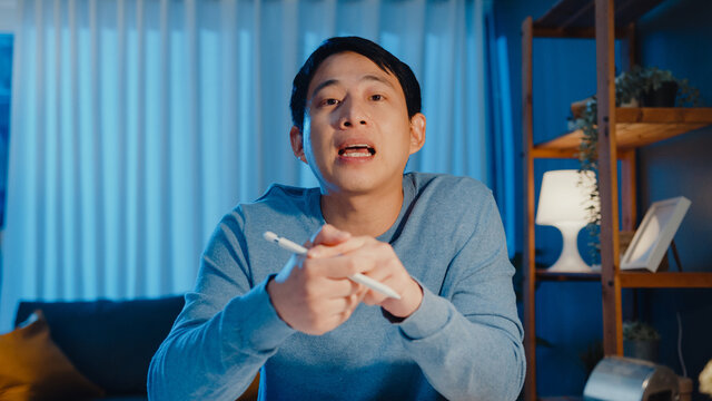 Asia businessman looking at camera focus online video call meeting assignment work with colleague on tablet in living room at home overtime at night, Work from home coronavirus pandemic concept.