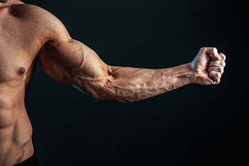 tense arm clenched into fist, veins, bodybuilder muscles on a dark background, isolate