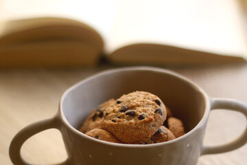 Bowl of chocolate chip cookies and open book on a table. Selective focus.