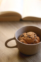 Bowl of chocolate chip cookies and open book on a table. Selective focus.
