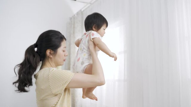 mother coming over to the crib and lifting her baby high up to check on butt is leaving to change the stinky diaper after doing a grimace for disgust at home