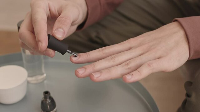 Close up of hands of unrecognizable young man applying grey nail polish on fingernails