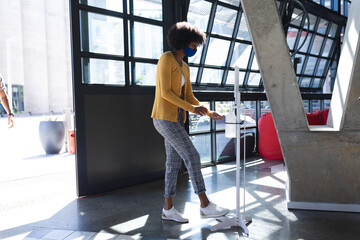 African american woman wearing face mask disinfecting hands