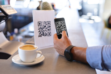 Mixed race man using smartphone and reading qr code in cafe