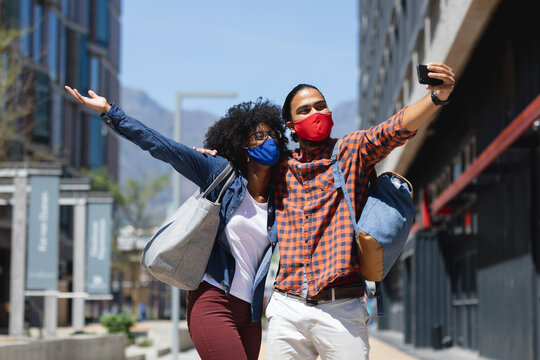 Mixed race man and african american woman wearing masks, embracing, taking selfie