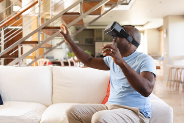 African american senior man gesturing while wearing vr headset sitting on the couch at home