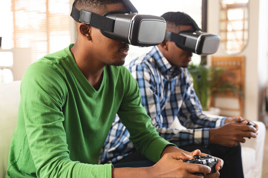 African american brothers wearing vr headset playing video games while sitting on the couch at home