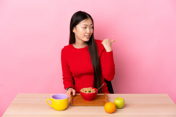 Young Chinese girl  having breakfast in a table pointing to the side to present a product