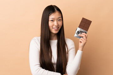 Young Chinese girl over isolated background taking a chocolate tablet and happy