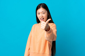 Young Chinese girl over isolated blue background with thumbs up because something good has happened