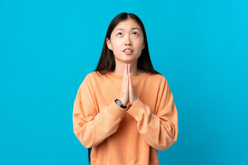 Young Chinese girl over isolated blue background keeps palm together. Person asks for something