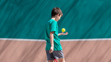 Kid tennis sport concept. Child boy tennis player playing and training with racket and ball against background of blue and orange tennis wall. copy space