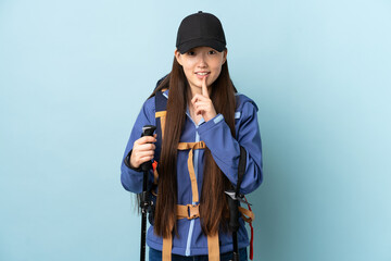 Young Chinese girl with backpack and trekking poles over isolated blue background showing a sign of silence gesture putting finger in mouth