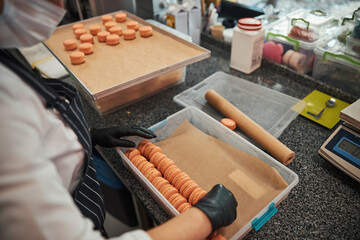 Attentive cook packing macaron desserts into a dry box - obrazy, fototapety, plakaty