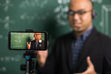 Indian young teacher man wearing headset teaching online video conference live stream by...